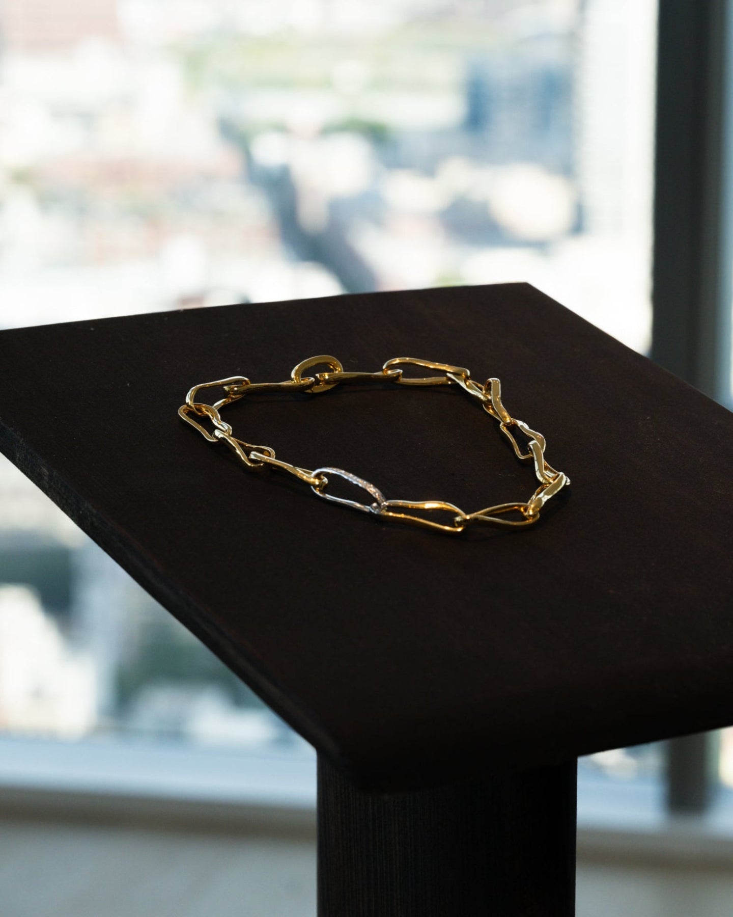 Gold bracelet on a black stand with a blurred window background