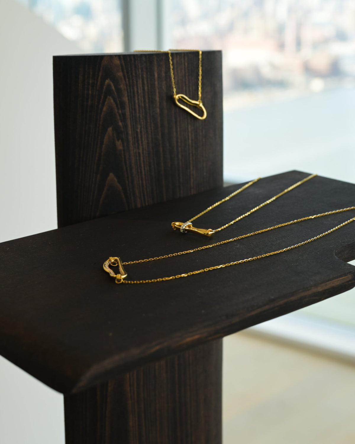 Gold necklace displayed on a dark wooden stand with a blurred cityscape in the background