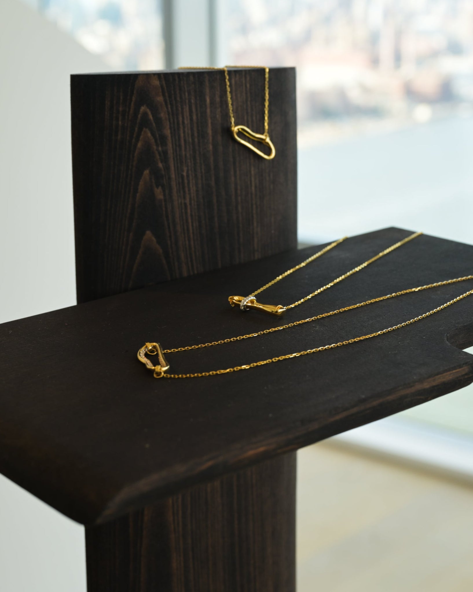 Gold necklace displayed on a dark wooden stand with a blurred cityscape in the background