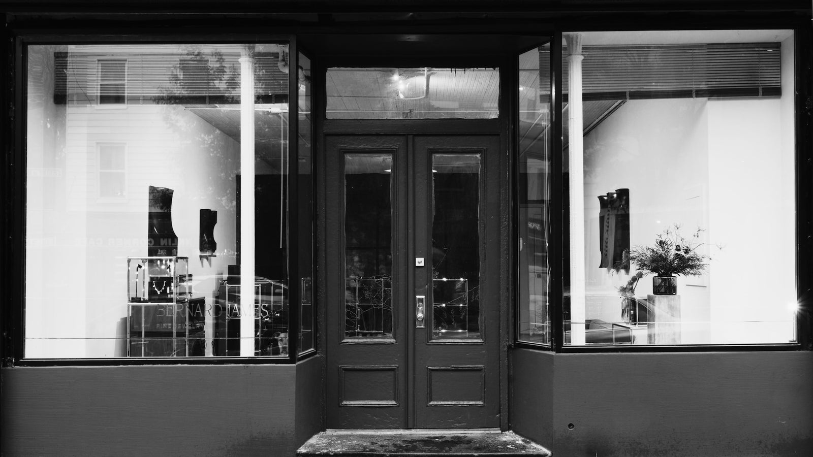 Black and white photo of a store front with large windows and glass doors.