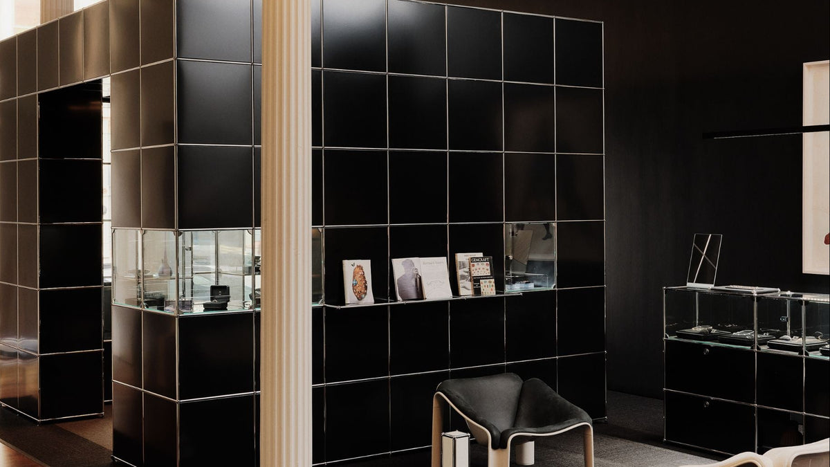 A modern interior space with a large black tiled partition wall, glass display cases, a black chair, and dark walls. No person or animal is present, and the scene appears to be a real environment rather than a clean isolated product shot.