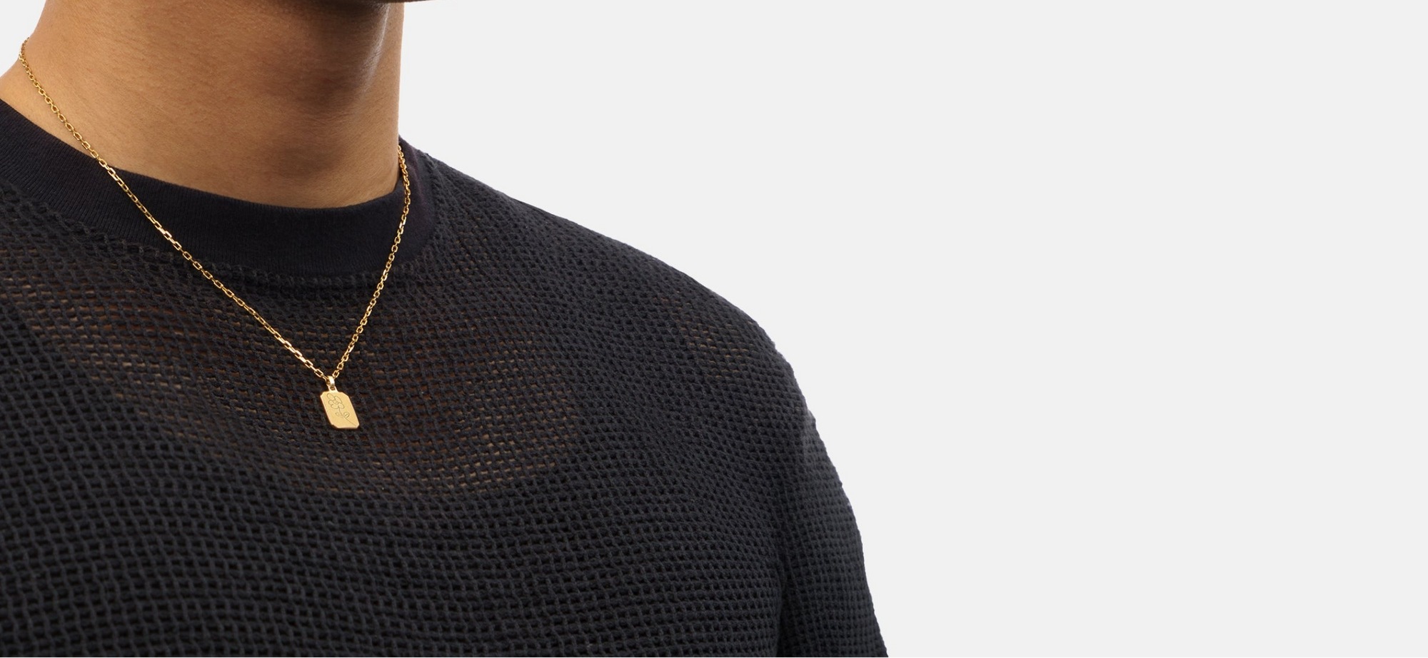 Person wearing a black textured shirt with a gold necklace on a light gray background