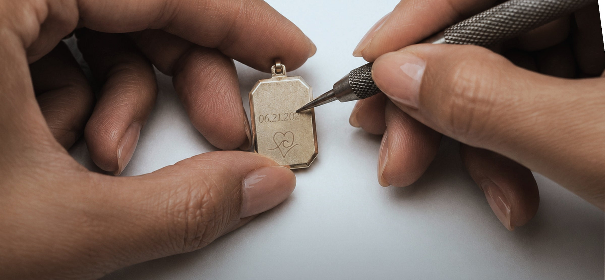 Person engraving a gold pendant with a tool on a white background